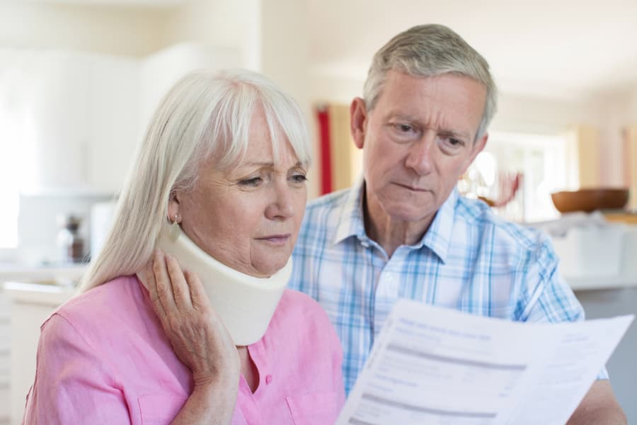 older woman with neck brace holding a document and husband standing near her