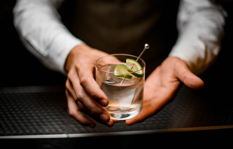 Close-up of hands of a male bartender holding a cocktail garnished with lime