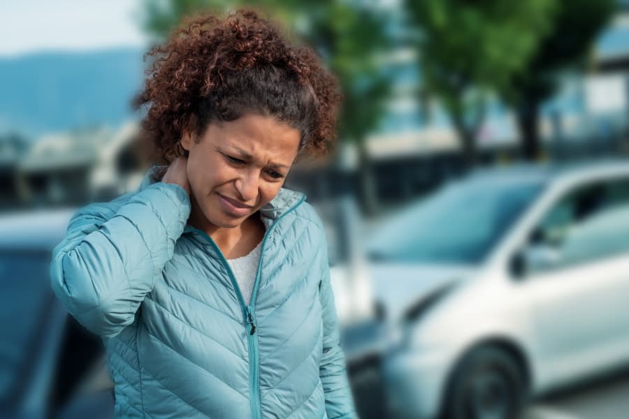 African American woman in a blue jacket holding her neck with a blurred car accident in the background