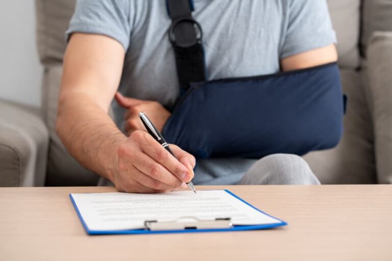 A close-up of a man with his arm in a sling signing a paper on a blue clipboard.