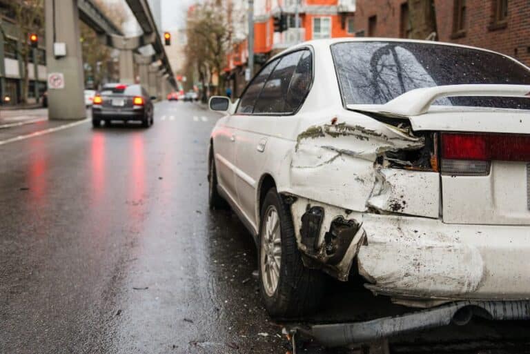 A sideswiped white car on a city street with a silver car speeding away.