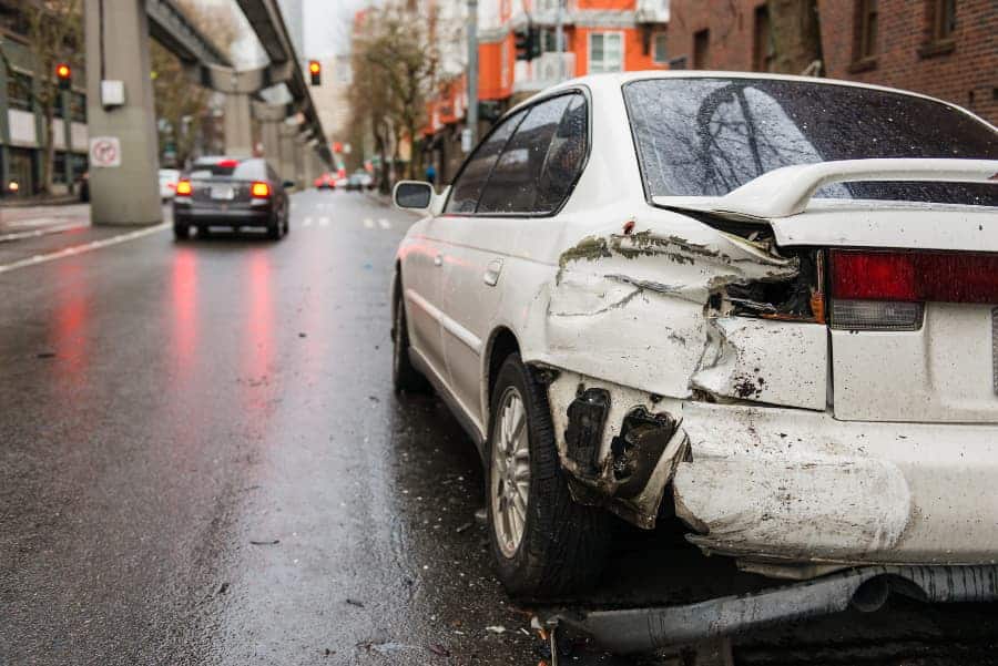 A sideswiped white car on a city street with a silver car speeding away.